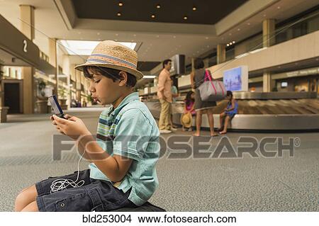 Picture - Boy playing on cell phone in airport. Fotosearch
