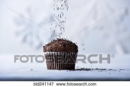 Stock Photo - Brown sprinkles falling on chocolate cupcake. Fotosearch