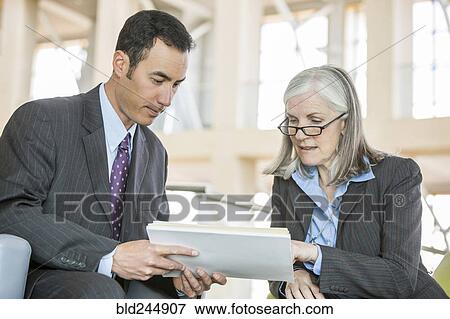 Business people reading paperwork in lobby View Large Photo Image Stock Photo - Business people reading paperwork in lobby. Fotosearch