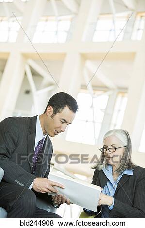Stock Photo - Business people reading paperwork in lobby. Fotosearch