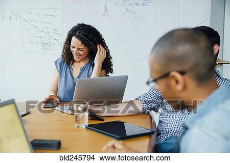 Picture - Business people using cell phones in meeting. Fotosearch