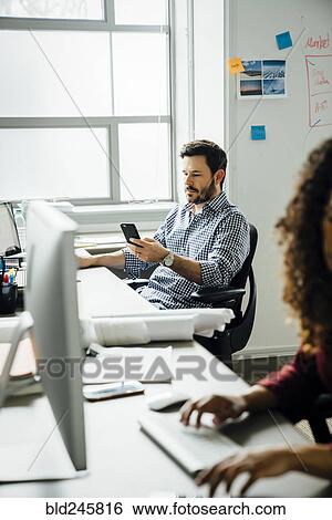Businessman texting on cell phone in office View Large Photo Image Stock Photograph - Businessman texting on cell phone in office. Fotosearch