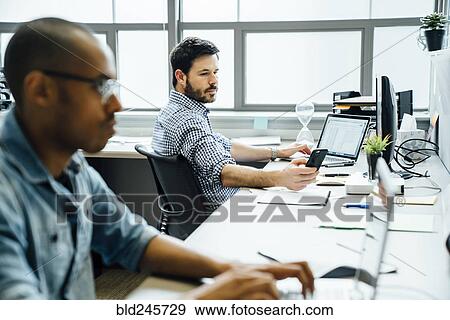 Stock Photo - Businessmen using technology in office. Fotosearch