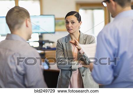 Businesswoman gesturing and talking to businessmen in office View Large Photo Image Stock Photo - Businesswoman gesturing and talking to businessmen in office. Fotosearch