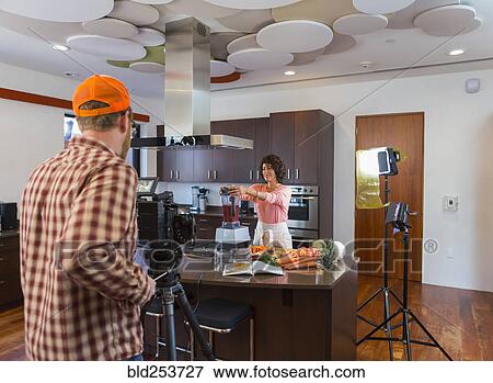 Stock Photo - Cameraman recording woman preparing smoothie in domestic kitchen. Fotosearch