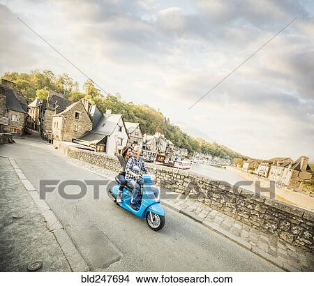 Carefree Caucasian couple riding blue motor scooter near river View Large Photo Image Picture - Carefree Caucasian couple riding blue motor scooter near river. Fotosearch