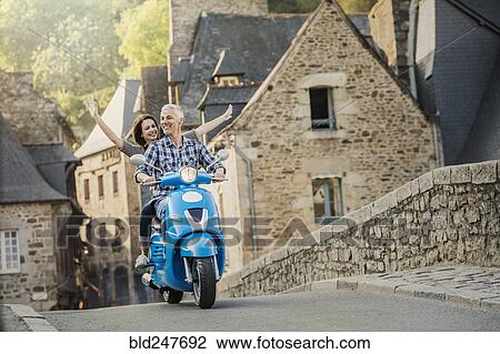 Stock Image - Carefree Caucasian couple riding blue motor scooter. Fotosearch