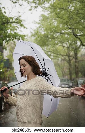Stock Photography - Carefree Caucasian woman holding an umbrella in the rain. Fotosearch