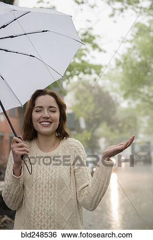Stock Photograph - Carefree Caucasian woman holding umbrella in rain. Fotosearch