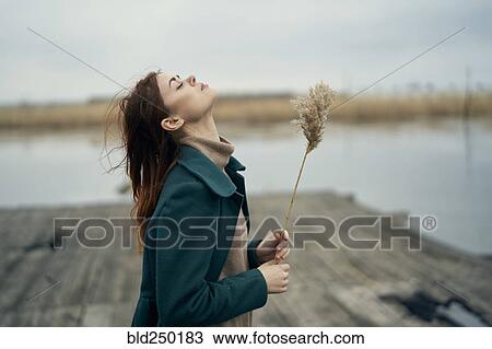 Carefree Caucasian woman standing on dock holding stalk of grass View Large Photo Image Stock Image - Carefree Caucasian woman standing on dock holding stalk of grass. Fotosearch