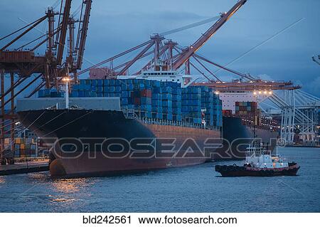 Stock Image - Cargo containers on freighter at shipping port near tugboat. Fotosearch
