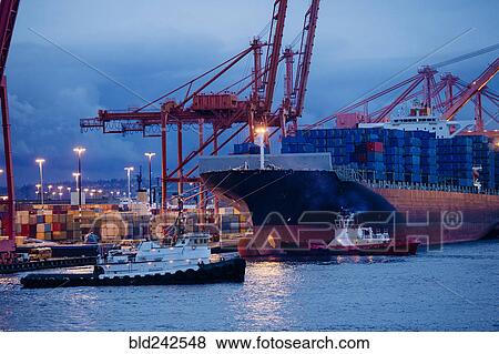 Stock Photo - Cargo containers on freighter at shipping port near tugboats. Fotosearch