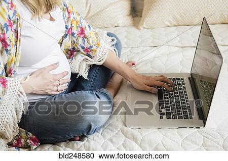 Caucasian and expectant mother using laptop on bed View Large Photo Image Stock Image - Caucasian and expectant mother using laptop on bed. Fotosearch