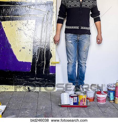 Stock Photo - Caucasian artist holding paint roller near painting. Fotosearch