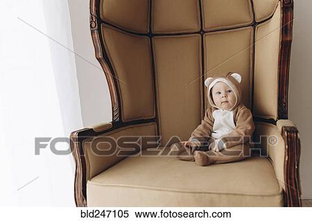 Stock Photography - Caucasian baby boy sitting in armchair wearing bear costume. Fotosearch