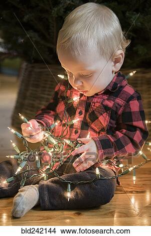 Caucasian baby boy sitting on floor wrapped in string lights View Large Photo Image Picture - Caucasian baby boy sitting on floor wrapped in string lights. Fotosearch
