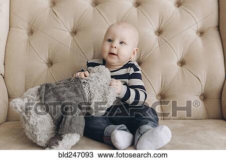 Caucasian baby boy sitting on love seat playing with teddy bear View Large Photo Image Stock Image - Caucasian baby boy sitting on love seat playing with teddy bear. Fotosearch