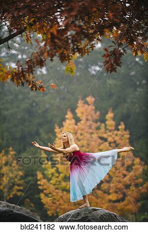 Stock Image - Caucasian ballerina dancing on rock in park. Fotosearch