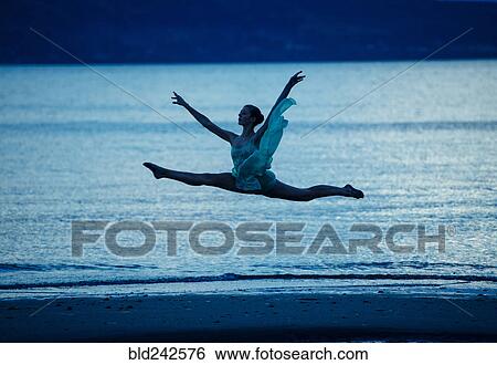 Stock Photograph - Caucasian ballerina jumping on beach at sunset. Fotosearch