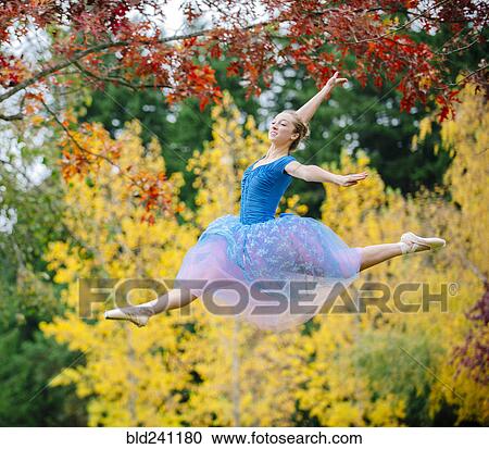 Stock Image - Caucasian ballerina leaping under branches in park. Fotosearch