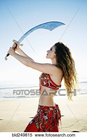 Stock Photography - Caucasian belly dancer holding sword on beach. Fotosearch