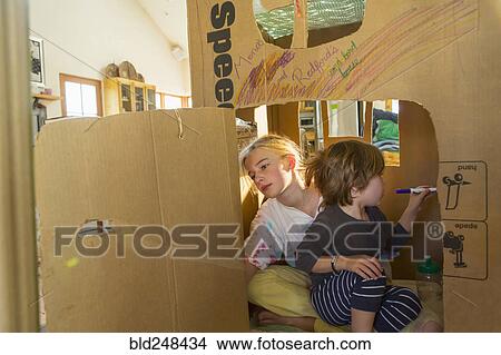 Picture - Caucasian boy and girl playing in cardboard house. Fotosearch