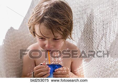 Stock Photography - Caucasian boy drinking juice through straw in hammock. Fotosearch