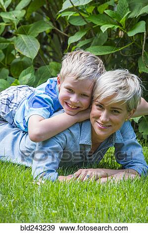 Stock Photo - Caucasian boy laying on back of mother in grass. Fotosearch