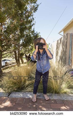 Stock Image - Caucasian boy photographing with camera near house. Fotosearch
