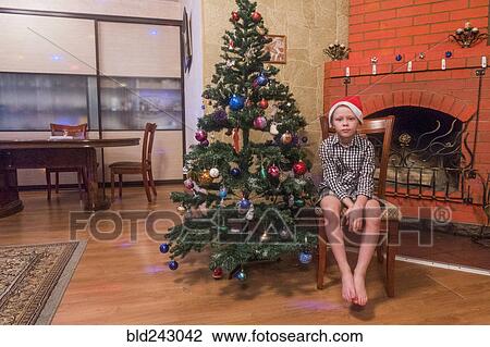Caucasian boy sitting on chair wearing Santa hat near Christmas tree View Large Photo Image Stock Image - Caucasian boy sitting on chair wearing Santa hat near Christmas tree. Fotosearch