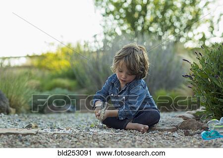 Stock Image - Caucasian boy sitting on ground smashing rocks with hammer. Fotosearch