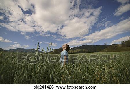 Stock Photograph - Caucasian boy standing in field looking up. Fotosearch