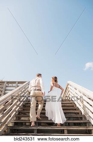 Stock Image - Caucasian bride and groom climbing wooden staircase. Fotosearch