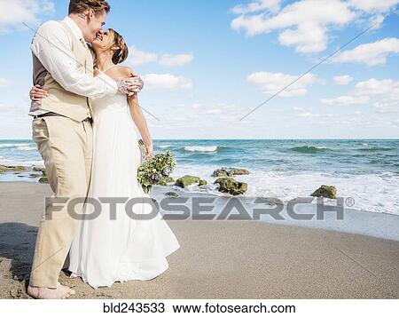 Stock Image - Caucasian bride and groom hugging on beach. Fotosearch