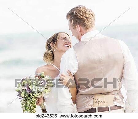 Stock Photograph - Caucasian bride and groom hugging on beach. Fotosearch