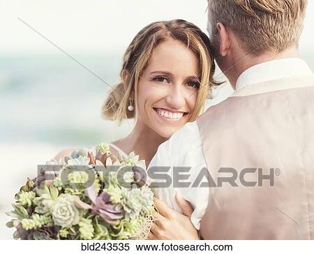 Stock Photography - Caucasian bride and groom hugging on beach. Fotosearch