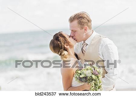 Stock Photo - Caucasian bride and groom kissing on beach. Fotosearch