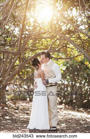 Stock Image - Caucasian bride and groom kissing under trees. Fotosearch