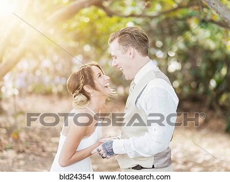 Stock Image - Caucasian bride and groom laughing outdoors. Fotosearch