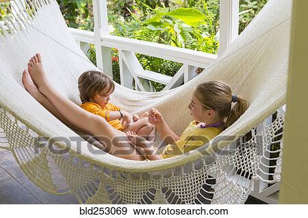Stock Photo - Caucasian brother and sister laying in hammock eating snack. Fotosearch