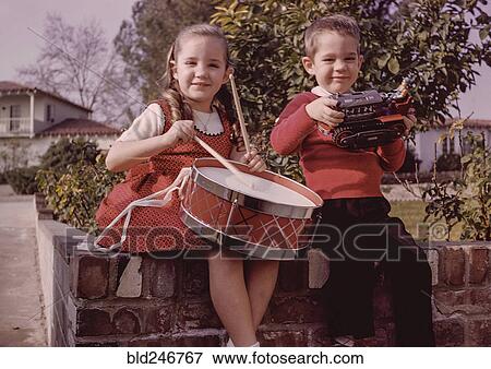 Stock Photo - Caucasian brother and sister sitting on brick wall with toys. Fotosearch