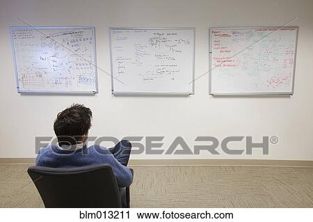 Stock Image - Caucasian businessman looking at whiteboards in conference room. Fotosearch