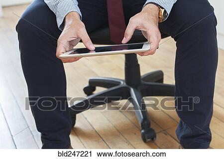 Stock Image - Caucasian businessman sitting on chair using digital tablet. Fotosearch