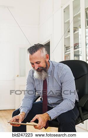 Stock Image - Caucasian businessman sitting on chair using digital tablet. Fotosearch