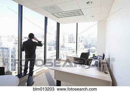 Stock Image - Caucasian businessman talking on cell phone in office. Fotosearch
