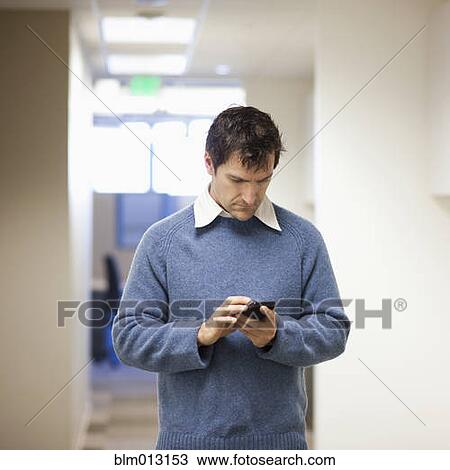 Stock Image - Caucasian businessman text messaging on cell phone in office. Fotosearch