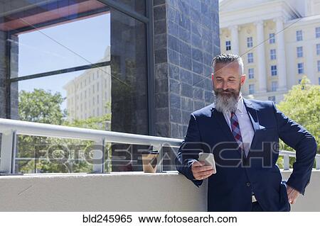 Stock Photography - Caucasian businessman texting on cell phone outdoors. Fotosearch