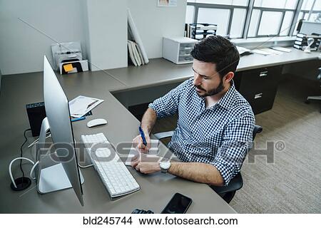 Picture - Caucasian businessman writing notes at a computer. Fotosearch
