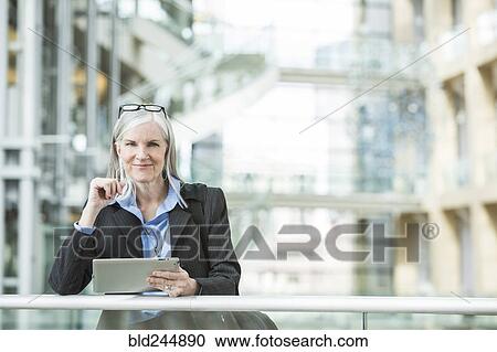 Stock Image - Caucasian businesswoman leaning on railing in lobby using digital tablet. Fotosearch