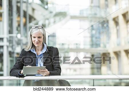Stock Photo - Caucasian businesswoman leaning on railing in lobby using digital tablet. Fotosearch